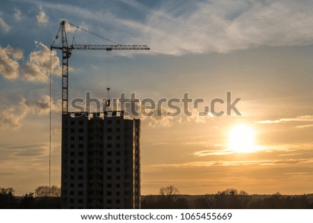 Tower cranes and unfinished multi-storey high near buildings under construction site in the rays of the setting sun of  beautiful sunset