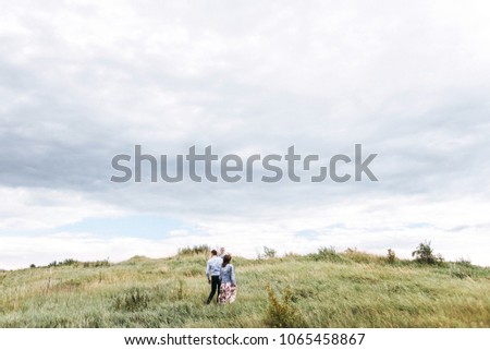Portrait of a happy family on a walk against the sky. Daughter in the arms of Mom and Dad. Family walking in the park in the grass. Happiness to be together.