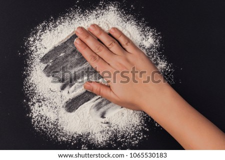 wheat flour and female hand on a black background