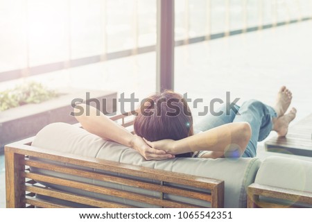 Relax business woman lifestyle at home sitting on modern chair in living room looking out of window toward beautiful cityscape downtown urban landscape city life w/ sunlight effect: Royalty-Free Stock Photo #1065542351