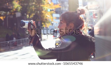 woman wearing warming clothes and scarf holding camera to take a photo with the happiness in winter while traveling oversea
