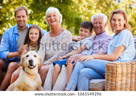 Three generation family sitting with pet dog in the garden Royalty-Free Stock Photo #1065549296