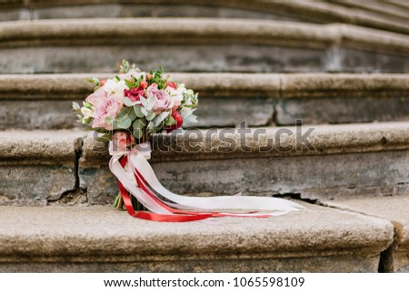 a wedding bouquet of roses and pions of berries and greens with pink and red ribbons stands on stone steps