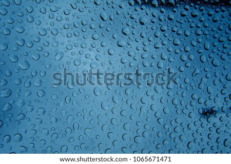Rain drops on a window glass in heavy rainy day and dark clouds.Drops of rain on glass.Rain drops on window glasses surface with cloudy background . Natural Pattern of raindrops isolated on cloudy 