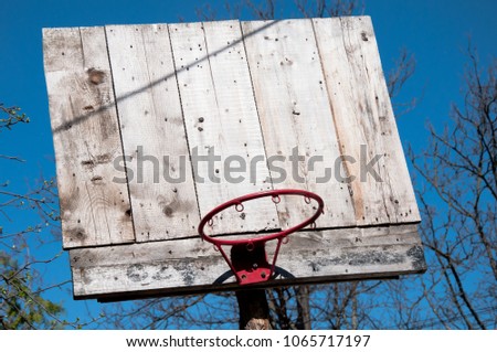 old wooden basketball board with red hoop without net and trees and blue sky as background