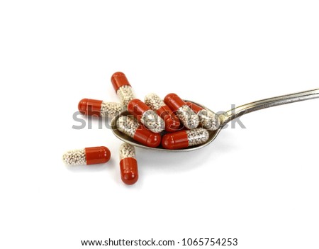 Red transparent capsule in a silver spoon isolated on white background.
