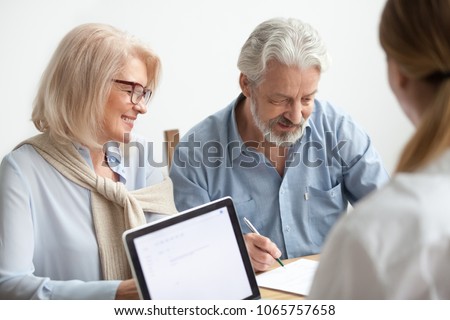 Happy senior couple about to sign document at meeting with financial advisor, older man agrees to put signature on contract making investment purchase, taking insurance, aged family in travel office