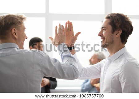 Smiling male colleagues giving high five in office, happy motivated young men coworkers celebrating victory, goal achievement win or successful teamwork, sharing good result, friends greeting concept Royalty-Free Stock Photo #1065757700