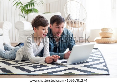 One of the biggest blessings in the world is to have parents to call mom and dad! Amazed son and father lying on the floor and watching a film on the laptop.