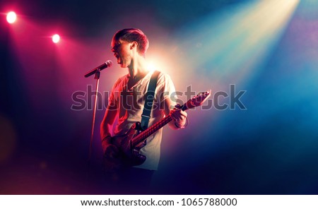 Rock singer with a guitar in stage lights Royalty-Free Stock Photo #1065788000