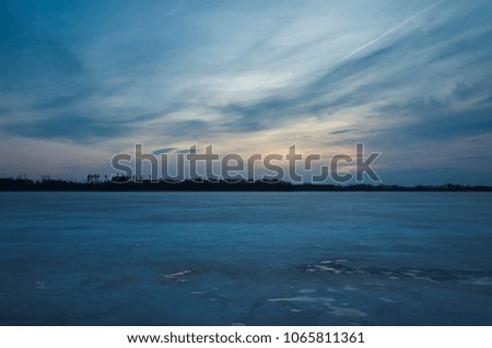 Beautiful nature and landscape photo of spring evening in Sweden Scandinavia Europe. Nice fresh blue dusk sky at sunset. Frozen lake with ice and trees at horizon. Calm, peaceful, joyful photo.