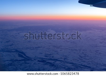 Aerial view from airplane window above land with snow and beautiful sunset