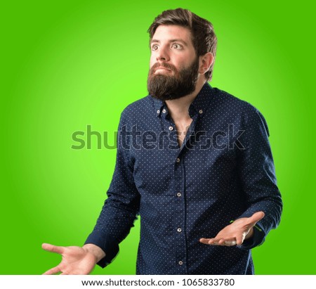 Young hipster man with big beard doubt expression, confuse and wonder concept, uncertain future over green background