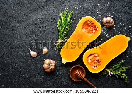 Halves of raw organic butternut squash with spices and ingredients for making on a black slate, stone or concrete background.Top view with copy space. Royalty-Free Stock Photo #1065846221