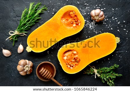 Halves of raw organic butternut squash with spices and ingredients for making on a black slate, stone or concrete background.Top view.