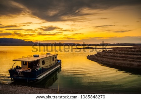 A houseboat moored to the muddy shores of the Lake Mead National Recreation Area, Nevada, at dusk with a dramatic and colorful cloudy sky - Holidays, tourism and vacation concept picture. Royalty-Free Stock Photo #1065848270