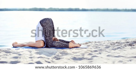 Wide picture of a woman practicing  Ear Pressure yoga Pose at the beach