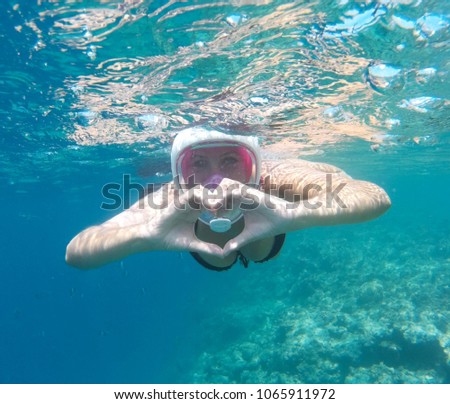 Young girl shows hands symbol heart underwater