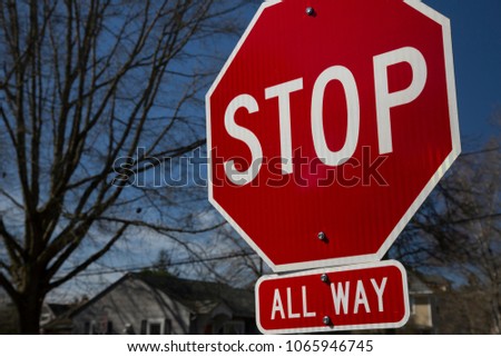 Stop All Way street sign with neighborhood, trees, and blue sky in background
