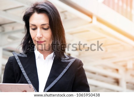 Business women working on tablet device and offices building background.