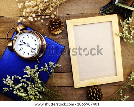 blank photo frame and alarm clock with dried flower top view on the table wooden background