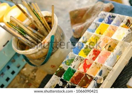 Paint brushes in the cup and palette water paints are on the table