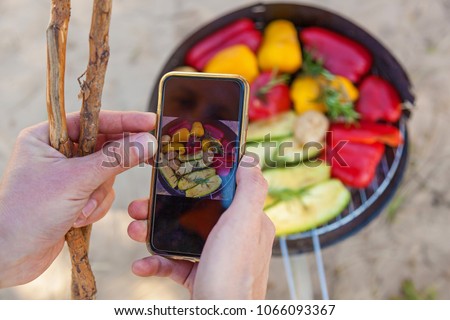 Man takes pictures on phone grilled vegetables.Vegetables red and yellow sweet pepper, mushrooms and zucchini roasted on a round barbecue