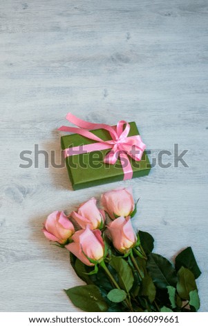 Bouquet of pink roses and gift box in green wrapping paper with pink ribbon on wooden background. Greeting card for Valentine's day, International women's day, mother's day