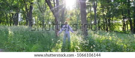 A young guy in a gray sports suit rejoices in the rising of the sun among the trees in the forest. Recreation during a sports run in the open air forest. The delight of a beautiful dawn