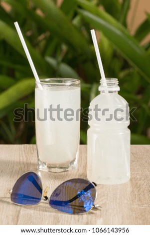 A glass and a bottle with a white drink on a table on a green background