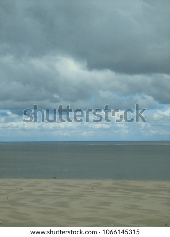 Beautiful abstract picture with the lines of gray cloudy sky, sea and beach, with a few walking people, at Texel, one of the Dutch islands