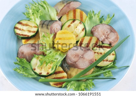 Slices of smoked mackerel and vegetables cooked on the grill (potatoes and zucchini). The appetizer is decorated with green onions and lettuce leaves. View from above. Close-up. Macro photography.
