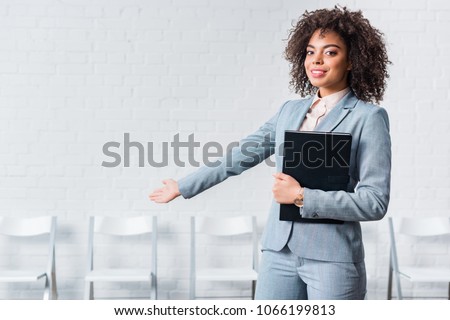 Young girl in suit holding folder and inviting to sit down on chair