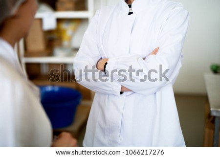Close up female worker in white cloths in a factory holding crossed arms.