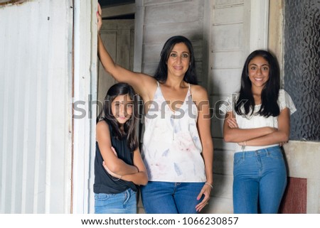 Outdoor portrait of an attractive mother and her daughters.
The smiling mother and the older sister in white top, the cute little girl in black top standing in front of the door.
 Royalty-Free Stock Photo #1066230857