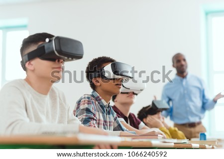 Multicultural schoolchildren using virtual reality headsets and african american teacher standing behind Royalty-Free Stock Photo #1066240592