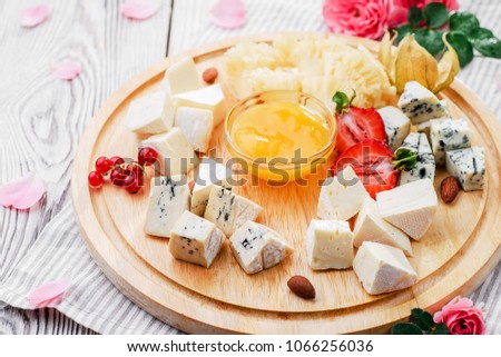 Romantic cheese plate Assortment of various types of cheese on wooden cutting board with pink flowers. Close up. seria of photo