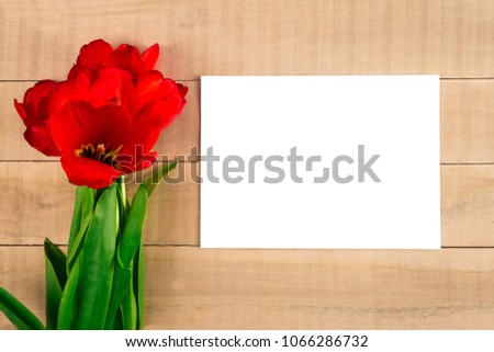 a bouquet of red tulips and a white sheet of paper on a wooden table