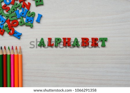 Developing accessories for children's creativity, wooden multicolored letters of the alphabet and lettering alphabet, colored pencils on a wooden background.