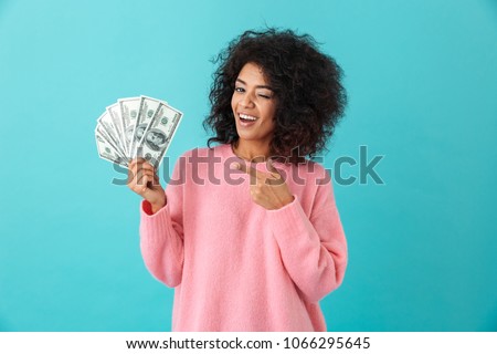 Portrait of american successful woman 20s with afro hairstyle holding lots of money dollar ï»¿banknotes isolated over blue background Royalty-Free Stock Photo #1066295645