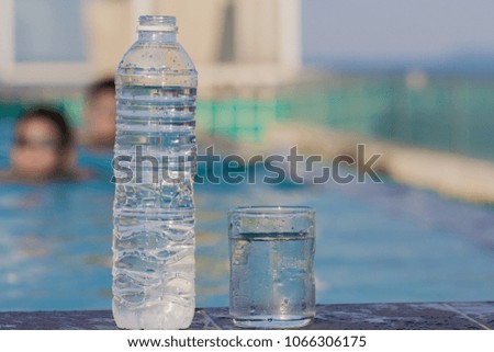 Glass of water and plastic water bottle by the pool.