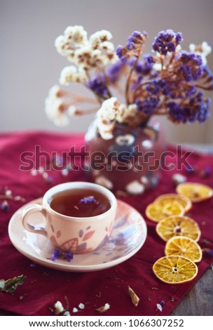 The vase with flowers, cup of tea  and pieces of mandarins  stand on the table