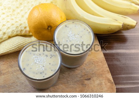 banana and tangerine smoothie is photographed on dark wooden background.