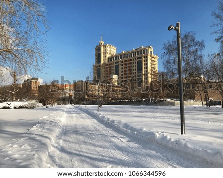 The snowy road leading to the multi-storey city building is lit by a bright winter sun.