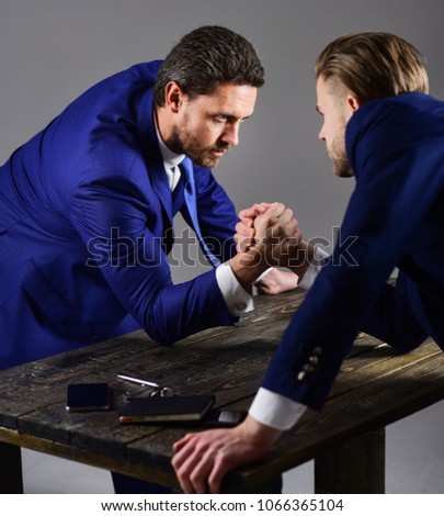 Businessmen fighting for leadership. Confrontation of business leaders. Men in suit or businessmen with tense faces compete in armwrestling on table on dark background. Business competition concept.