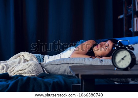Image of dissatisfied woman with insomnia lying on bed next to alarm clock at night