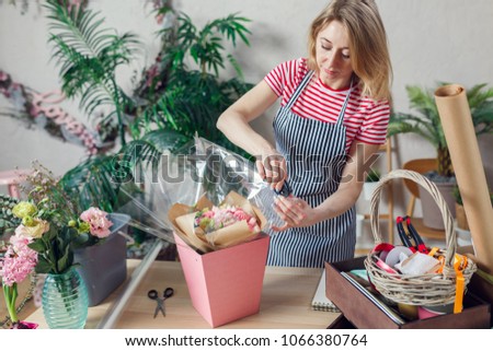 Portrait of female florist with stapler decorating floral composition at table with flowers, boxes