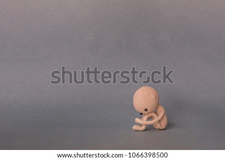 A toy man on a gray background with copy space. Cute amigurumi. Presentation PowerPoint or Keynote. Motivational phrase. A person sits, holding his feet with his hands, sad or crying