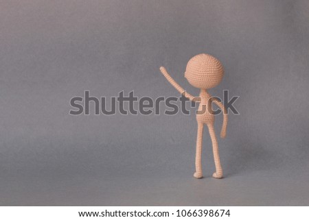 A toy man on a gray background with copy space. Cute amigurumi. Presentation PowerPoint or Keynote. Motivational phrase. The man stands with his back and presses on the object on the left