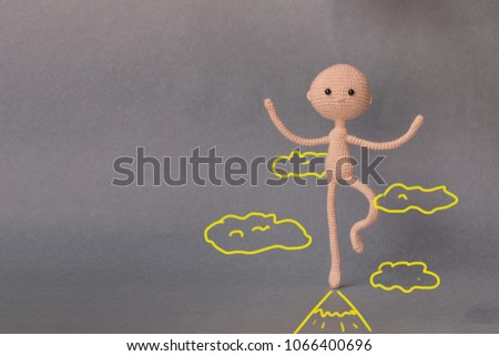 A toy man on a gray background with copy space. Presentation PowerPoint or Keynote. Motivational phrase. A sketch is drawn on top of the photo.A man stands on one foot at the peak top of the mountain